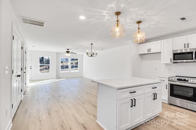 kitchen featuring decorative light fixtures, appliances with stainless steel finishes, white cabinetry, and a center island