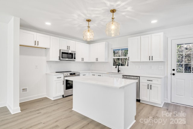 kitchen featuring white cabinetry, appliances with stainless steel finishes, hanging light fixtures, a kitchen island, and sink