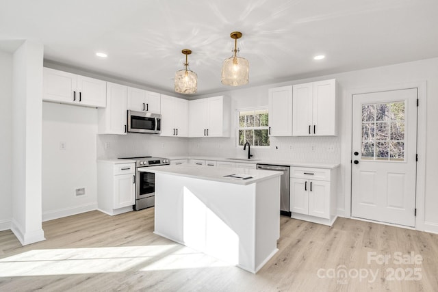 kitchen with decorative light fixtures, appliances with stainless steel finishes, white cabinetry, and a kitchen island