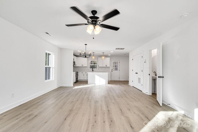 unfurnished living room with light wood-type flooring and ceiling fan with notable chandelier