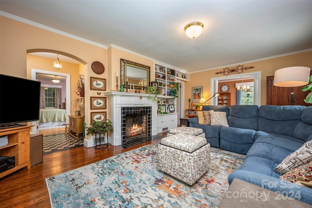 living room featuring a tile fireplace, dark wood-type flooring, a notable chandelier, and crown molding