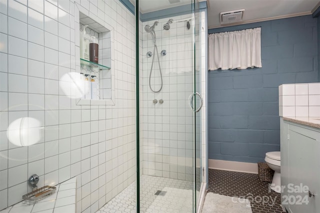 bathroom featuring toilet, tile walls, vanity, and a shower with shower door