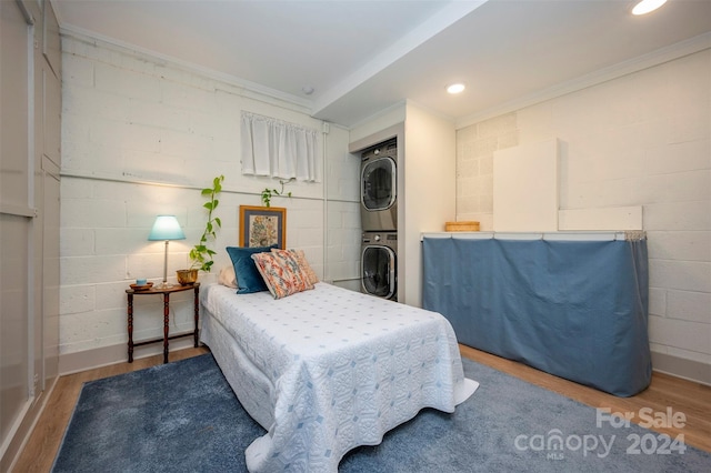 bedroom featuring stacked washing maching and dryer, hardwood / wood-style floors, and crown molding