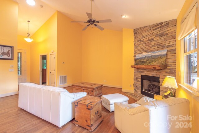 living room with light hardwood / wood-style flooring, a stone fireplace, high vaulted ceiling, and ceiling fan