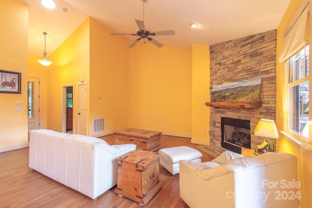 living room with high vaulted ceiling, a stone fireplace, and light hardwood / wood-style floors