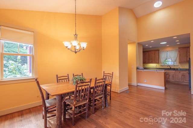 dining area featuring dark wood-type flooring, high vaulted ceiling, sink, and an inviting chandelier