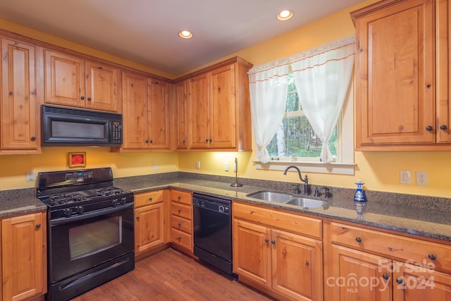 kitchen featuring dark stone countertops, dark hardwood / wood-style flooring, sink, and black appliances