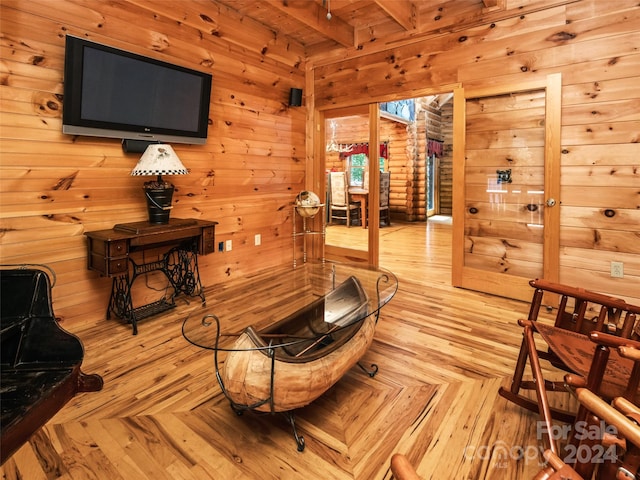 sitting room with beamed ceiling, light parquet flooring, and wooden walls