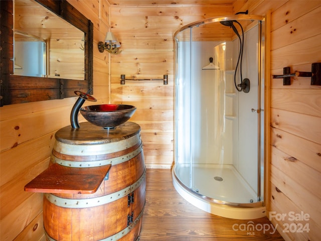 bathroom with hardwood / wood-style floors, vanity, a shower with door, and wood walls