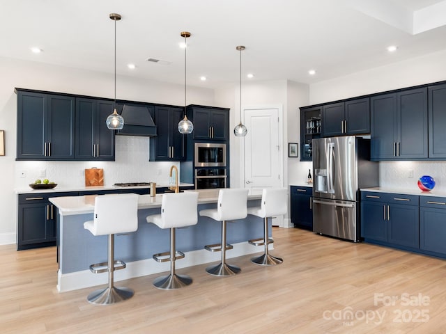 kitchen with stainless steel appliances, premium range hood, hanging light fixtures, a kitchen island with sink, and a breakfast bar