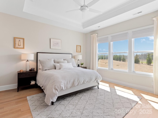 bedroom with ceiling fan, crown molding, a tray ceiling, and light hardwood / wood-style flooring