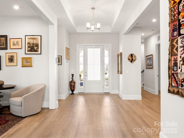 foyer featuring light hardwood / wood-style flooring, a raised ceiling, and a notable chandelier