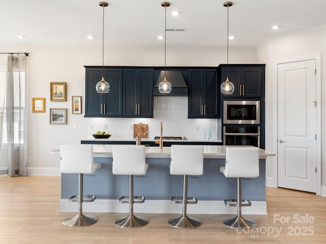 kitchen with hanging light fixtures, a kitchen island with sink, appliances with stainless steel finishes, and a kitchen bar