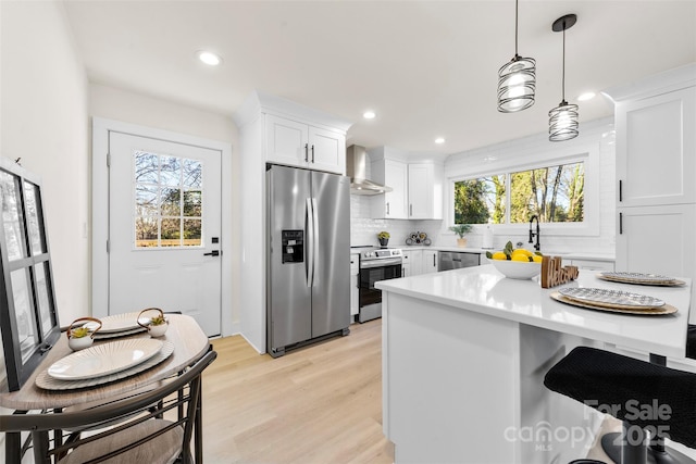 kitchen featuring wall chimney exhaust hood, decorative light fixtures, appliances with stainless steel finishes, white cabinets, and backsplash