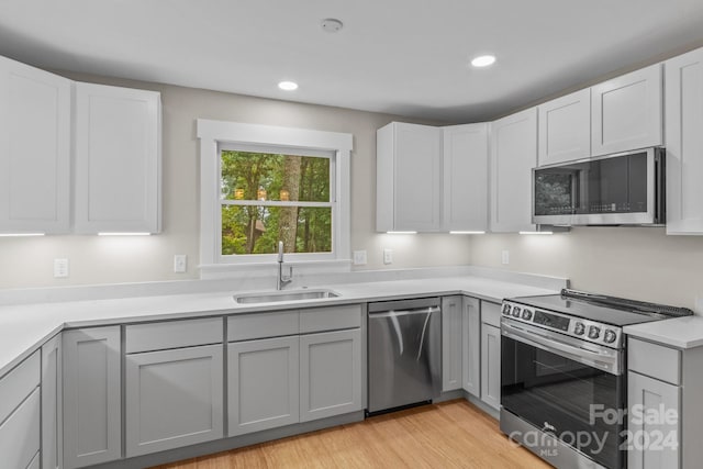 kitchen with sink, appliances with stainless steel finishes, gray cabinetry, white cabinets, and light wood-type flooring