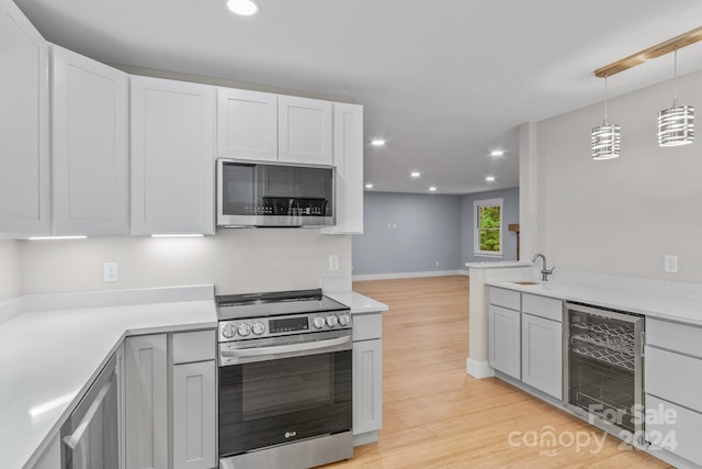 kitchen featuring stainless steel appliances, beverage cooler, hanging light fixtures, sink, and light hardwood / wood-style floors