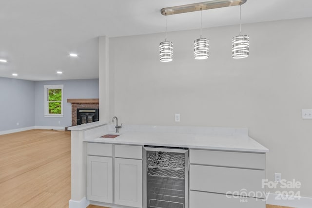 kitchen featuring wine cooler, sink, a brick fireplace, hanging light fixtures, and light wood-type flooring