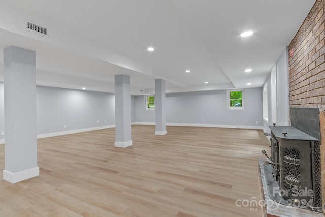 basement featuring brick wall, a wealth of natural light, a brick fireplace, and light hardwood / wood-style floors