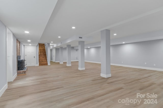 basement with brick wall, a fireplace, and light hardwood / wood-style floors