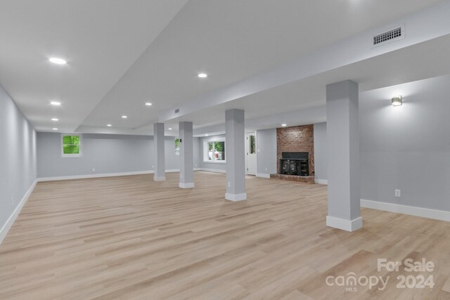 basement featuring light hardwood / wood-style flooring, a fireplace, and brick wall