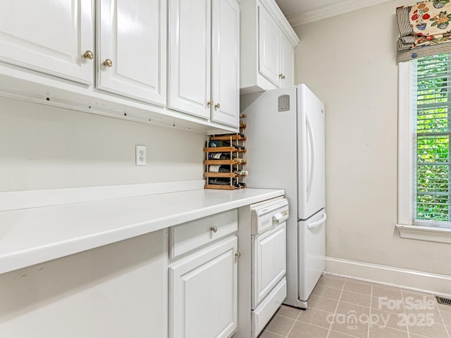 kitchen with a healthy amount of sunlight, light tile patterned floors, white cabinetry, and ornamental molding