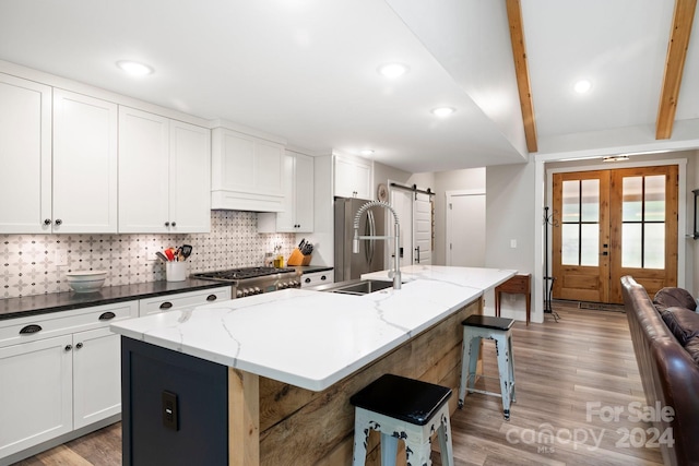 kitchen with light wood-type flooring, range, decorative backsplash, and an island with sink