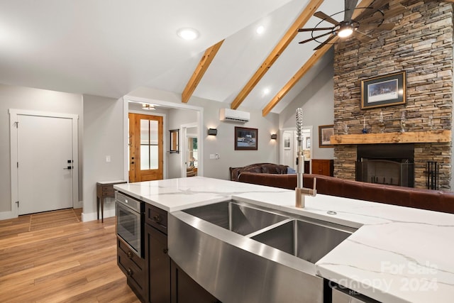 kitchen featuring light wood-type flooring, a wall unit AC, light stone countertops, a fireplace, and beamed ceiling