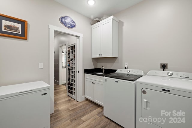 clothes washing area with sink, cabinets, light hardwood / wood-style floors, and washer and clothes dryer