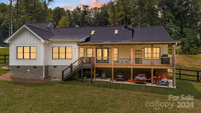 back house at dusk featuring a patio area and a lawn