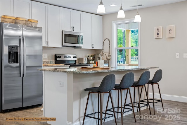 kitchen featuring pendant lighting, light stone countertops, appliances with stainless steel finishes, light hardwood / wood-style floors, and white cabinetry