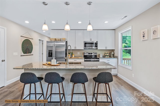 kitchen featuring white cabinets, light stone counters, an island with sink, and appliances with stainless steel finishes