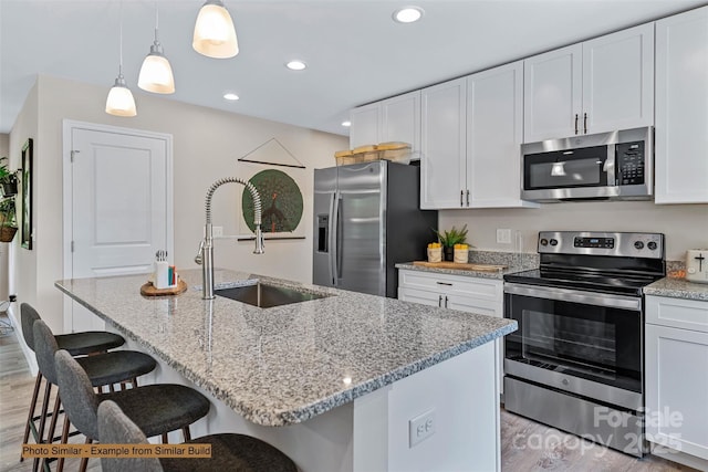 kitchen featuring stainless steel appliances, an island with sink, pendant lighting, light hardwood / wood-style floors, and white cabinets