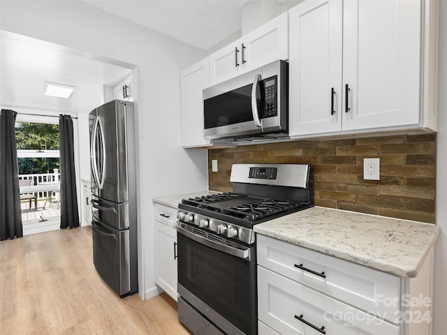 kitchen with backsplash, stainless steel appliances, light stone counters, white cabinets, and light wood-type flooring