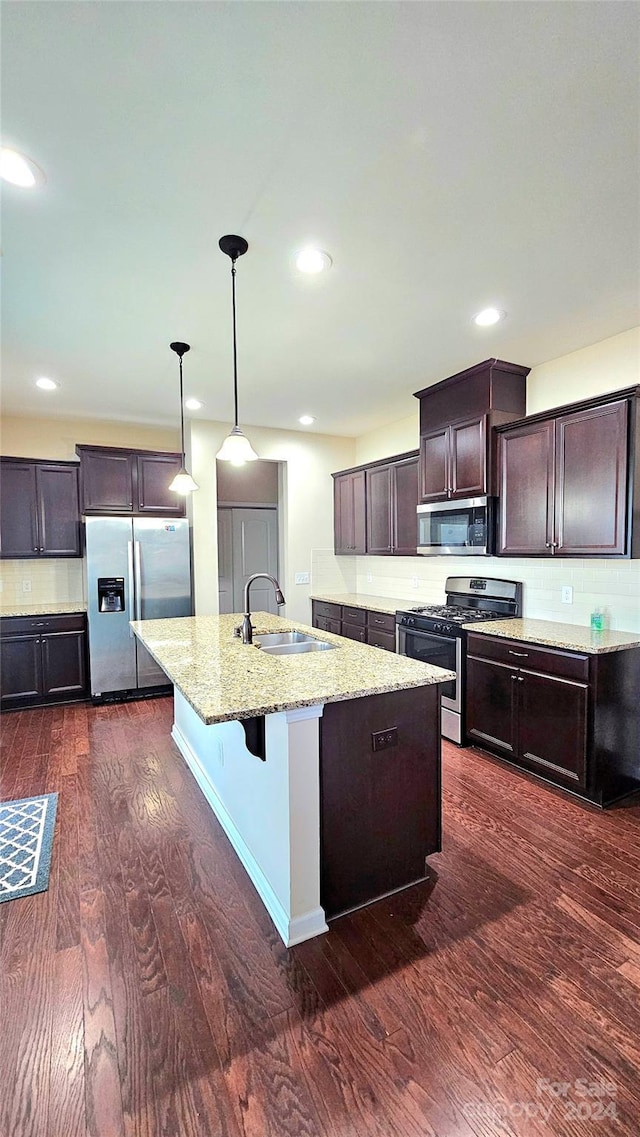 kitchen with a sink, light stone counters, dark wood finished floors, appliances with stainless steel finishes, and decorative backsplash