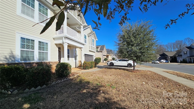 view of side of property with a residential view, a balcony, driveway, stone siding, and a garage