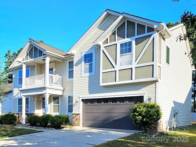 view of front of home with an attached garage, driveway, stone siding, and a balcony