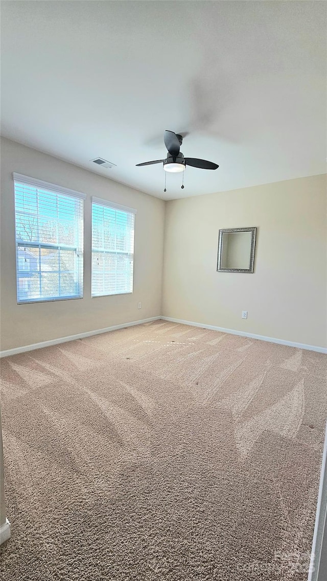 carpeted empty room with visible vents, baseboards, and ceiling fan