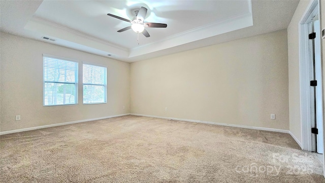 carpeted spare room featuring ceiling fan, a tray ceiling, ornamental molding, visible vents, and baseboards