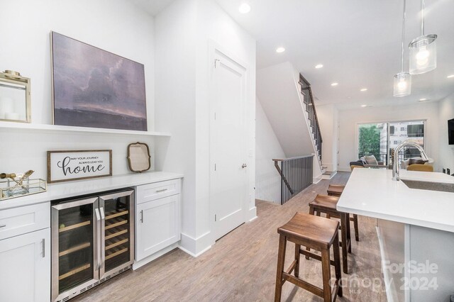 bar with light wood-type flooring, decorative light fixtures, white cabinetry, sink, and wine cooler