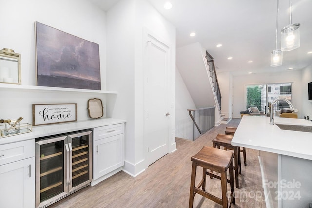 bar featuring wine cooler, light hardwood / wood-style flooring, pendant lighting, sink, and white cabinets