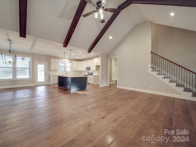 unfurnished living room with ceiling fan with notable chandelier, high vaulted ceiling, beamed ceiling, and light hardwood / wood-style floors