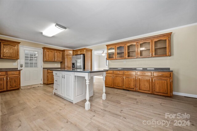 kitchen with stainless steel fridge, light wood-type flooring, a kitchen island, a breakfast bar area, and crown molding