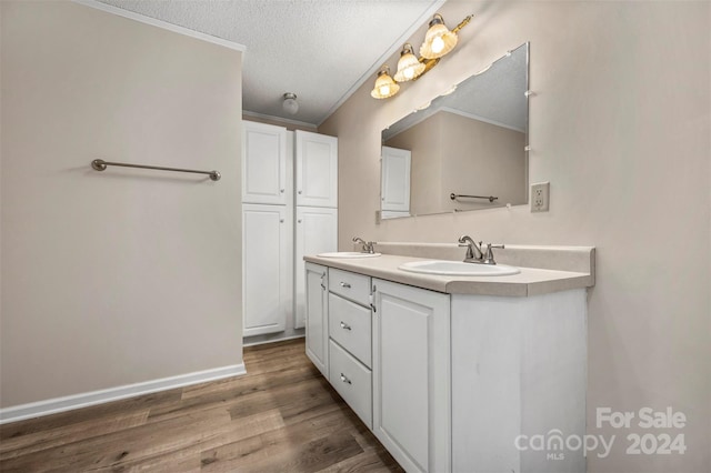 bathroom with a textured ceiling, crown molding, hardwood / wood-style floors, and double sink vanity