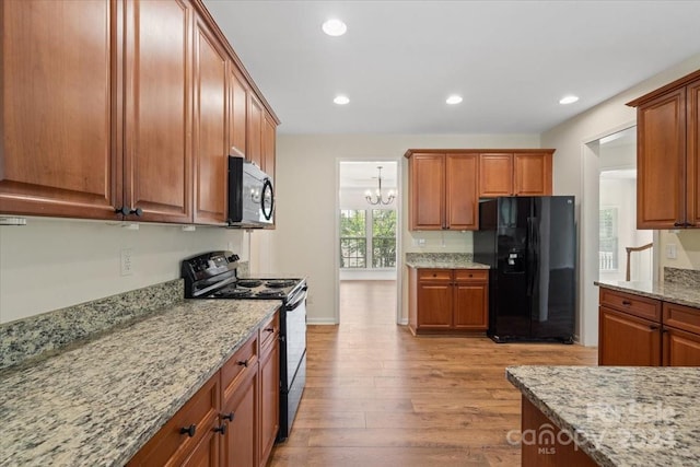 kitchen with light stone counters, a notable chandelier, black appliances, and light hardwood / wood-style floors