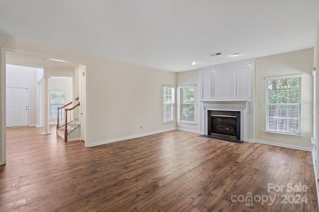 unfurnished living room featuring dark wood-type flooring, a healthy amount of sunlight, and ornate columns