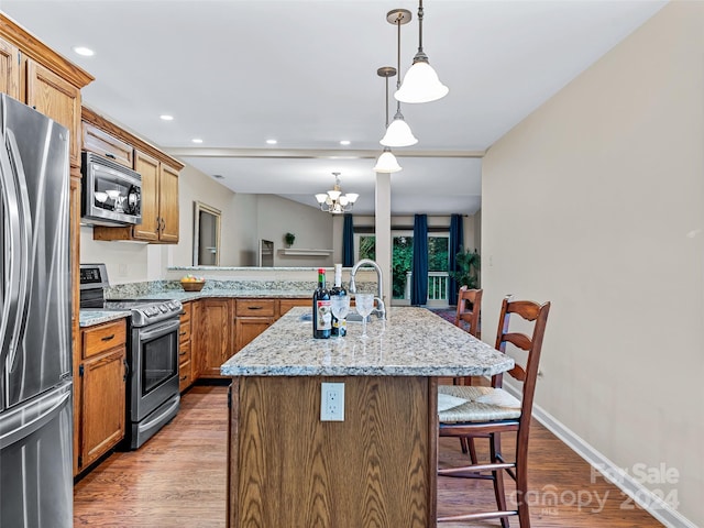 kitchen with light stone counters, stainless steel appliances, a sink, wood finished floors, and a kitchen breakfast bar