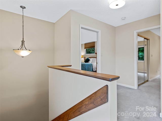 corridor with light carpet, a textured ceiling, and baseboards