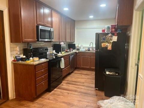 kitchen featuring tasteful backsplash, sink, light hardwood / wood-style flooring, and black appliances