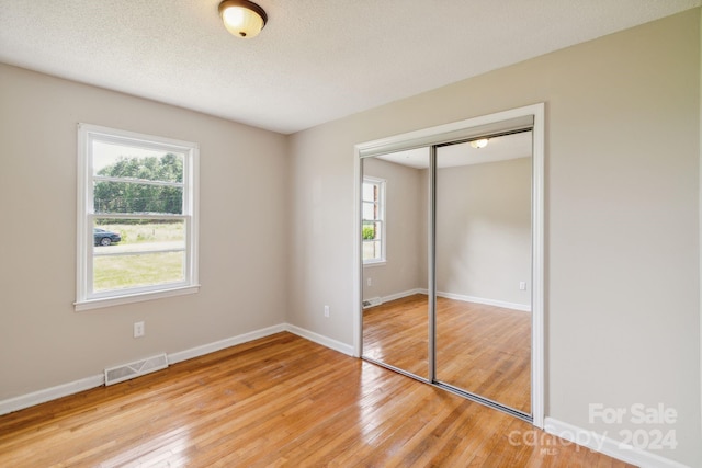 unfurnished bedroom with light hardwood / wood-style flooring, a closet, and a textured ceiling