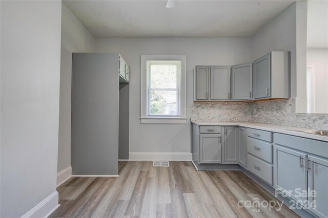 kitchen with gray cabinets, backsplash, and light hardwood / wood-style flooring